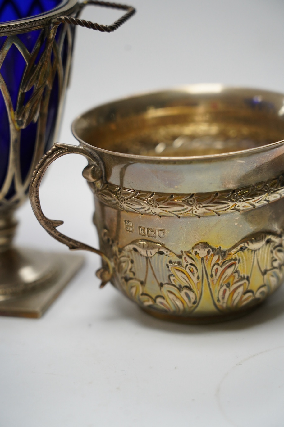 An Edwardian repousse silver porringer, Daniel & John Welby, London, 1905, height 73mm, together with a late Victorian silver two handled sugar vase with blue glass liner, London, 1895. Condition - fair